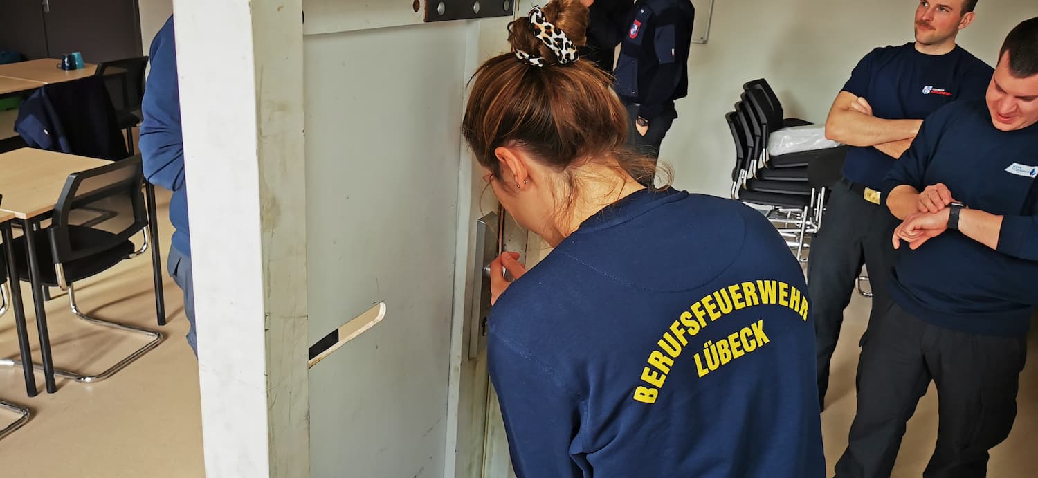 Eine Feuerwehr Anwärterin versucht im Lehrgangsraum eine Tür zu öffnen.